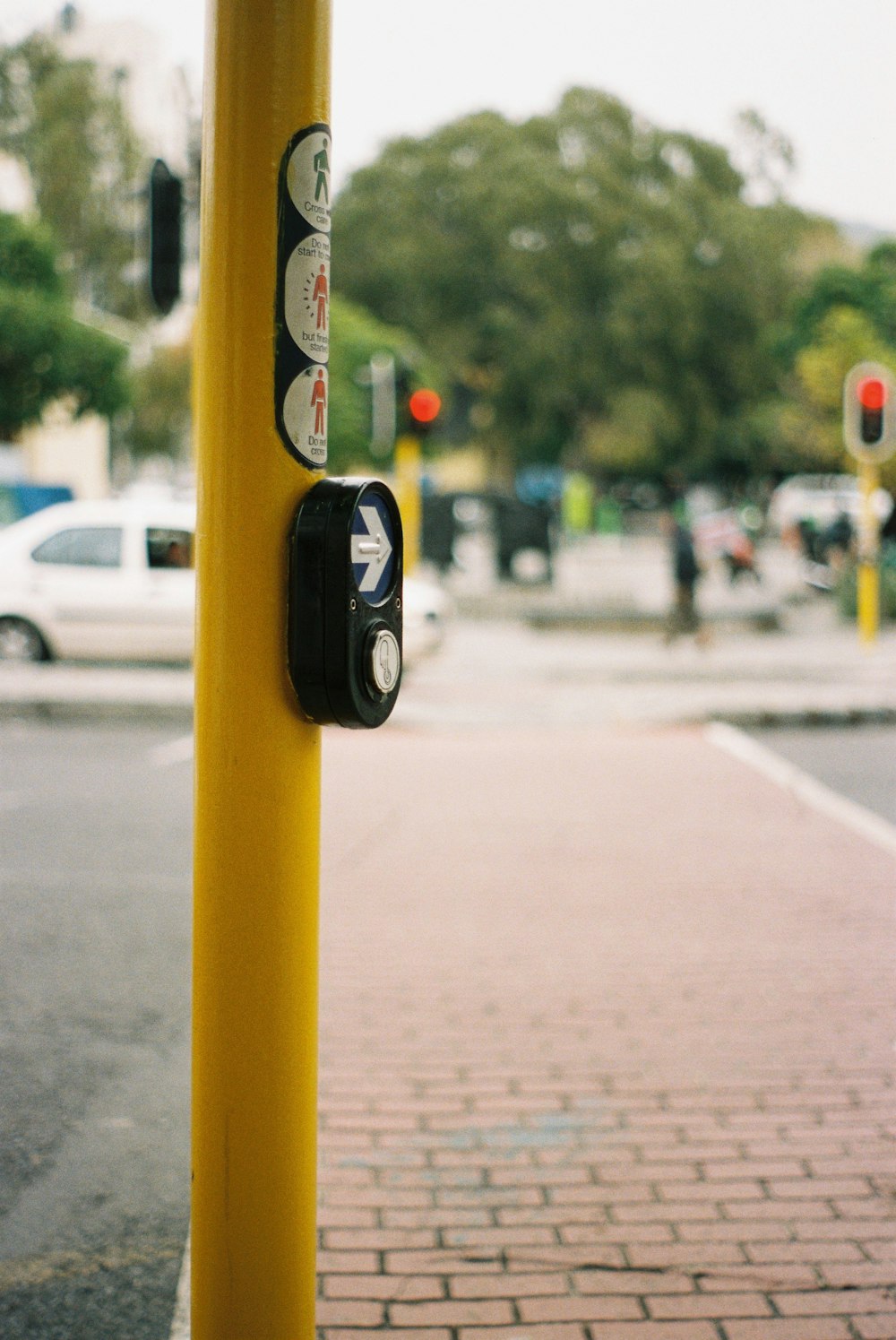 a yellow pole with a button on it on a city street
