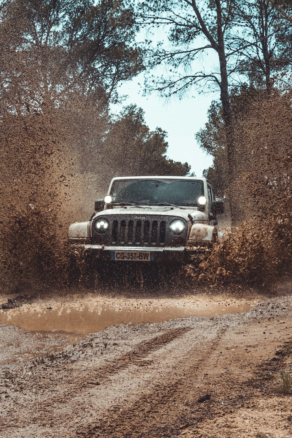 a jeep driving through a mud puddle on a dirt road