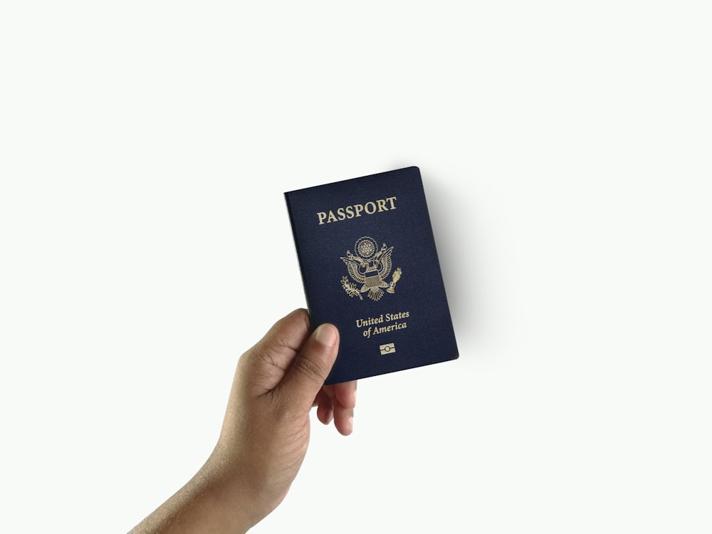 Una mano sosteniendo un pasaporte sobre un fondo blanco