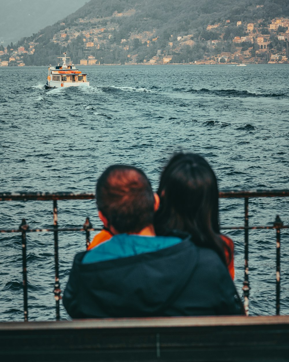 a man and a woman sitting on a bench looking at a boat in the water