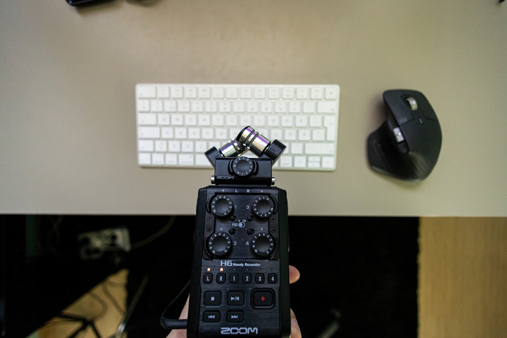 a hand holding a remote control in front of a keyboard