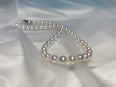 A string of lustrous white pearls is elegantly arranged on a smooth, satin-like fabric that has a soft, gentle sheen. The pearls are perfectly round and evenly spaced, reflecting light subtly and creating a luxurious, classic aesthetic.
