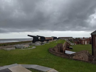 a grassy area next to a body of water under a cloudy sky