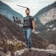 A man stands on a rock, holding a professional camera rig. He wears casual clothing and seems to be in a mountainous landscape with greenery in the background. The scene conveys a sense of adventure and filmmaking in nature.