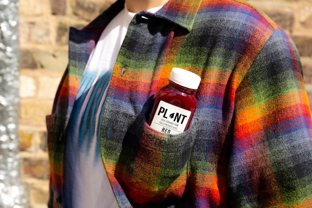 a man wearing a plaid jacket and holding a bottle of plum juice