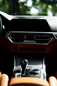 A modern car interior featuring a sleek dashboard with digital displays and a central console. The design has a luxurious feel with leather upholstery and chrome accents. The gear shifter and control dial are prominently positioned.