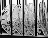 Decorative glass plates featuring intricate floral and geometric patterns are arranged in a row behind vertical black bars, with strong contrasts creating a prominent texture.