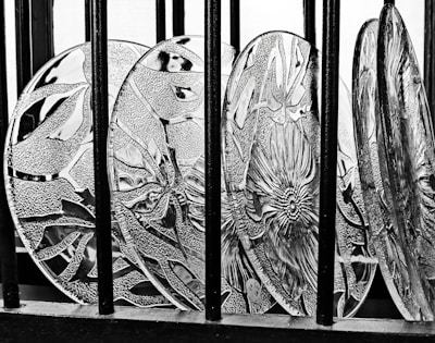 Decorative glass plates featuring intricate floral and geometric patterns are arranged in a row behind vertical black bars, with strong contrasts creating a prominent texture.
