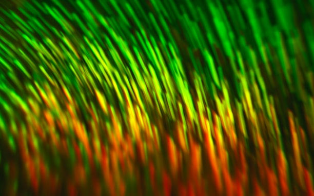 A dynamic abstract pattern featuring flowing streaks of vibrant green, yellow, and orange colors, creating an impression of movement and energy.