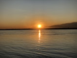 Sunset over a tranquil horizon with warm golden light reflecting on water.