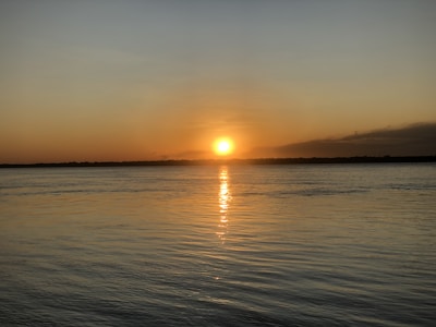Sunset over a tranquil horizon with warm golden light reflecting on water.