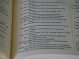 A close-up view of an open book, revealing text passages with poetic and religious themes. The page features numbered verses and italicized text, suggesting it might be a page from a Bible or other religious text.
