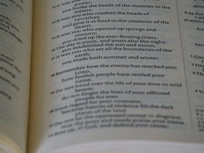 A close-up view of an open book, revealing text passages with poetic and religious themes. The page features numbered verses and italicized text, suggesting it might be a page from a Bible or other religious text.