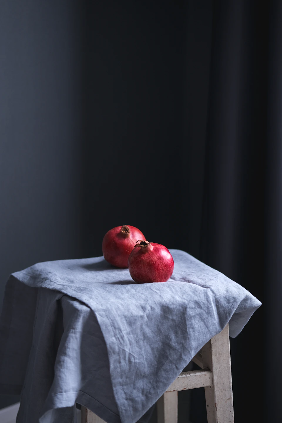 Two red pomegranates on a white wooden stool against dark gray background