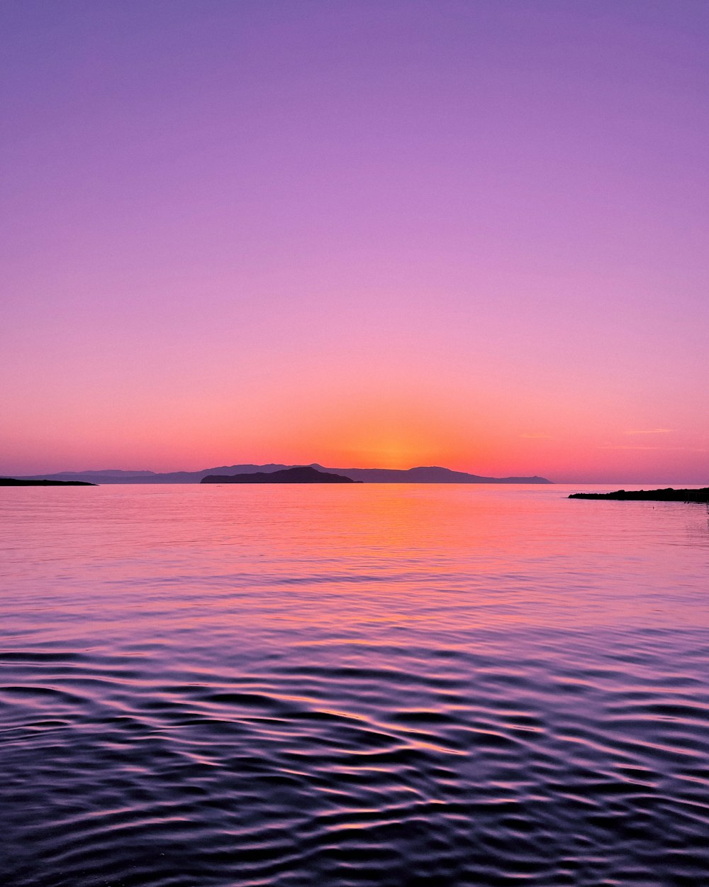 the sun is setting over the water with a small island in the distance