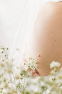 A close-up of a pregnant belly surrounded by delicate, small white flowers. The soft focus on the flowers in the foreground and the gentle lighting create a peaceful and dreamy atmosphere.