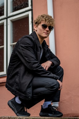 photography poses for men,how to photograph young adult portrait; a man in a black jacket and sunglasses sitting on a step
