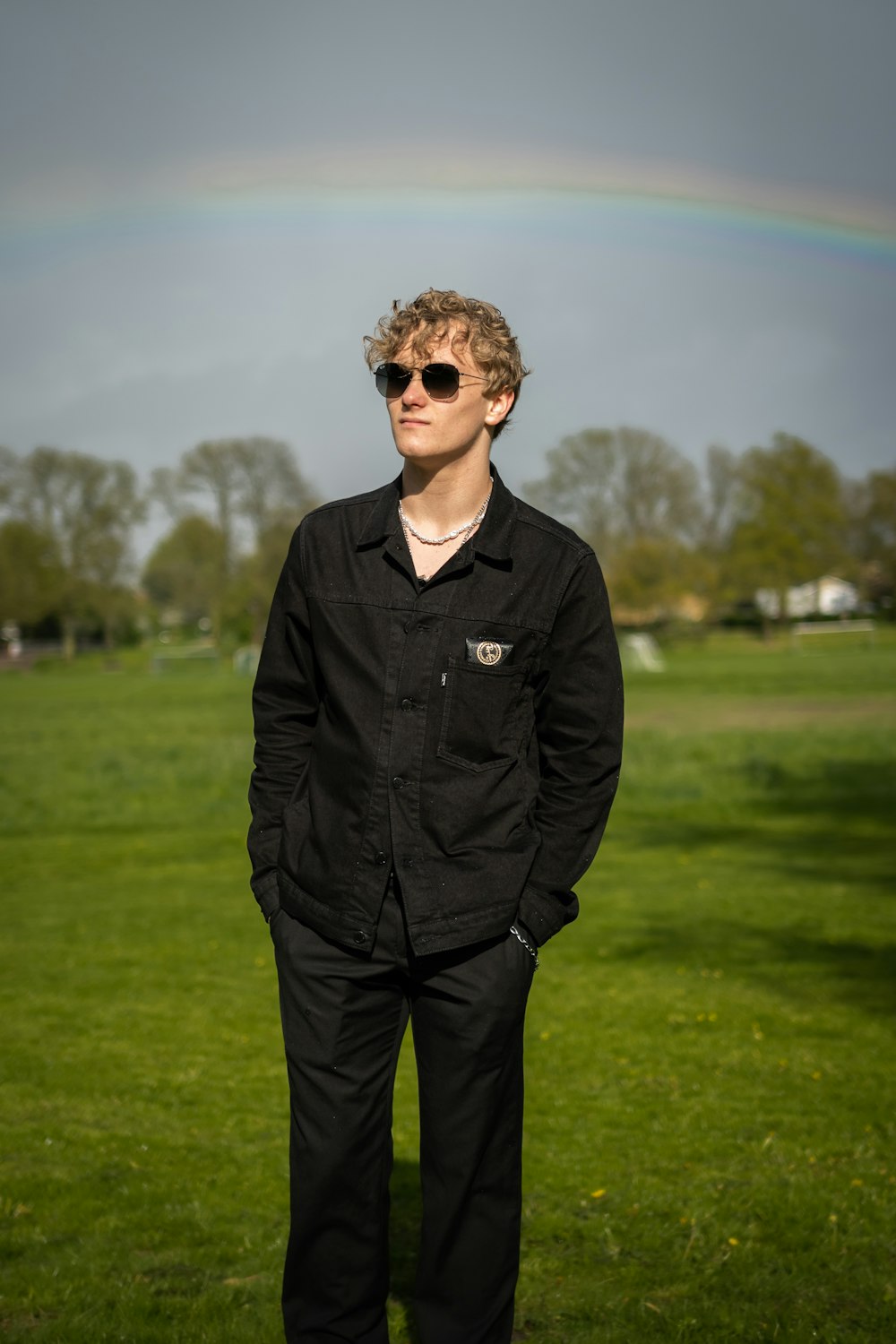 a man standing in a field with a rainbow in the background