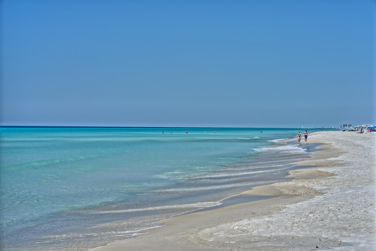 A beach with crystal clear waters with people walking along the coast of Destin Florida