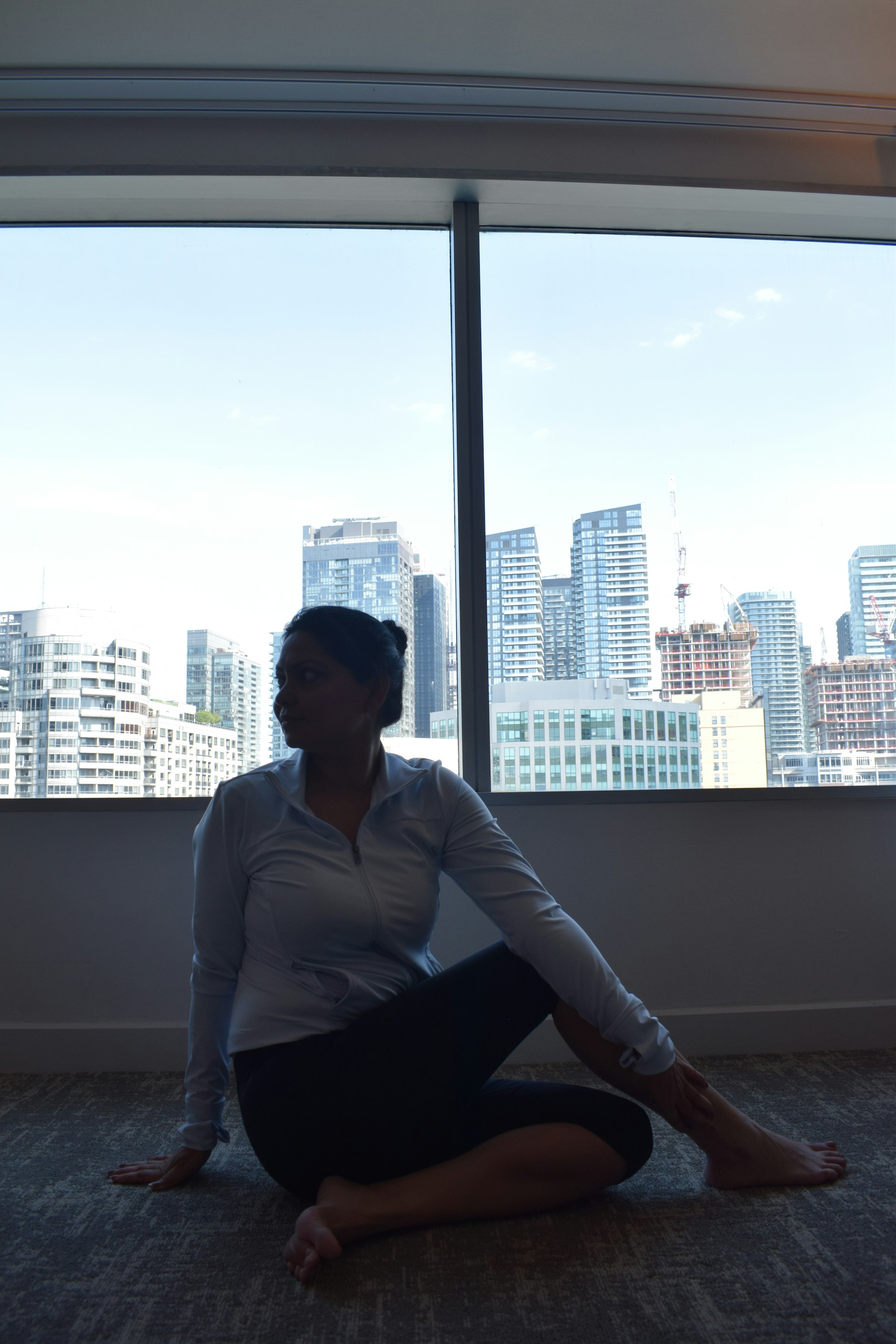 An instructor guiding a student through personalized Pilates exercises near large windows showing the city outside.