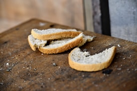 Several slices of white bread are scattered on a worn, wooden surface. The surroundings appear rustic, with the bread showing a simple, homemade quality.