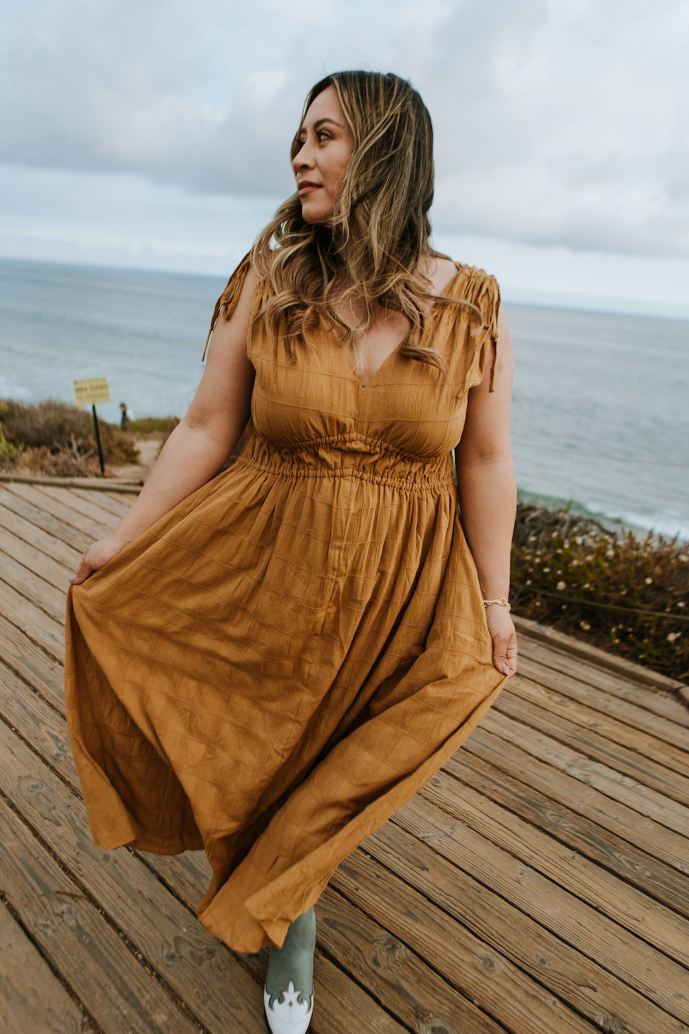 a woman in a brown dress standing on a wooden deck