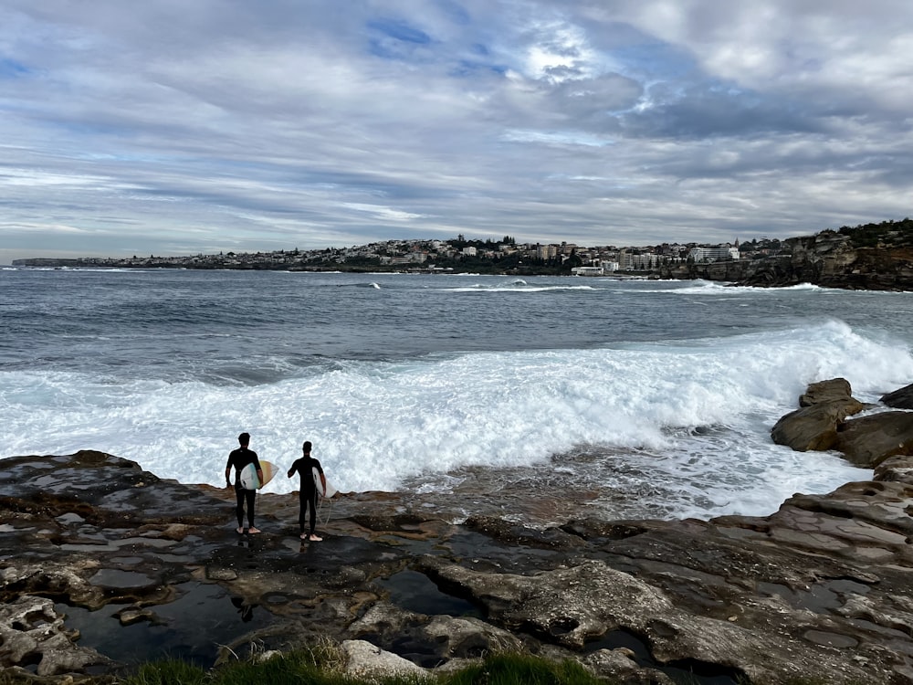 a couple of people standing on top of a rocky beach