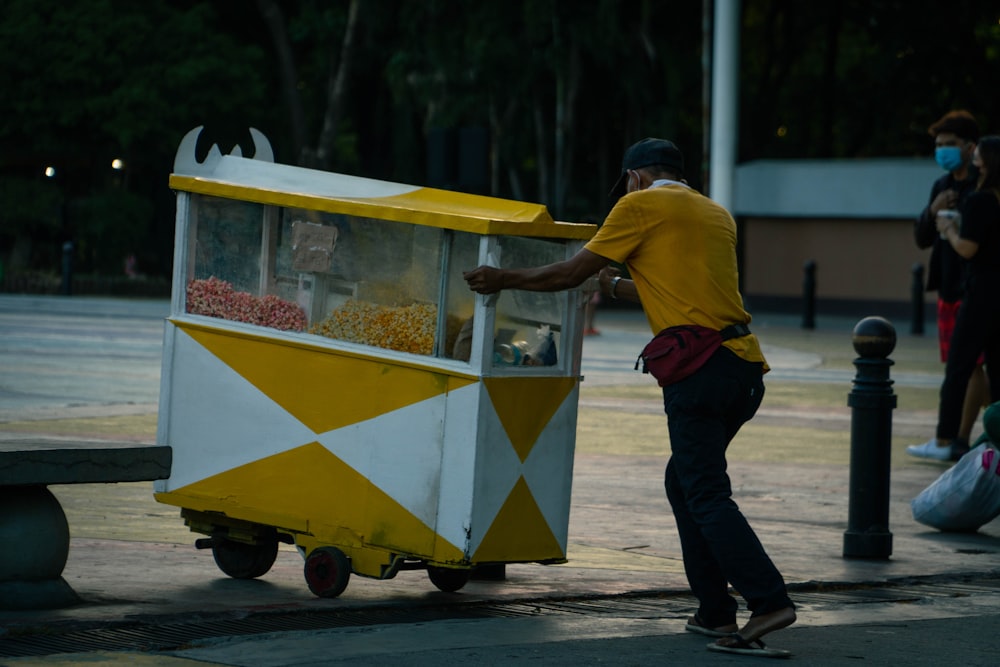 um homem empurrando um carrinho amarelo e branco cheio de doces