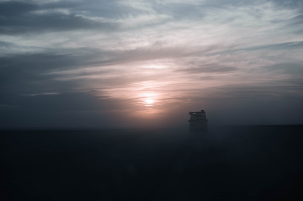 a truck driving through a field under a cloudy sky