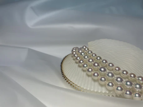 Close-up of a delicate freshwater pearl necklace resting on soft beige fabric with gentle gold accents.