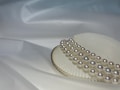 A close-up view of a string of lustrous pearls artistically arranged on top of a textured white surface, possibly a seashell, with a soft and smooth draped fabric as the background.