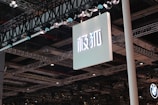 A large sign with Asian characters is suspended from a ceiling structure composed of multiple metal beams and spotlights. The lighting fixtures are prominently visible, casting illumination over the area.
