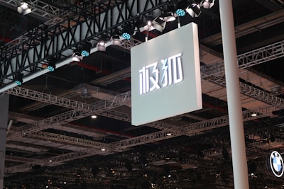 A large sign with Asian characters is suspended from a ceiling structure composed of multiple metal beams and spotlights. The lighting fixtures are prominently visible, casting illumination over the area.