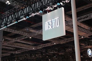 A large sign with Asian characters is suspended from a ceiling structure composed of multiple metal beams and spotlights. The lighting fixtures are prominently visible, casting illumination over the area.