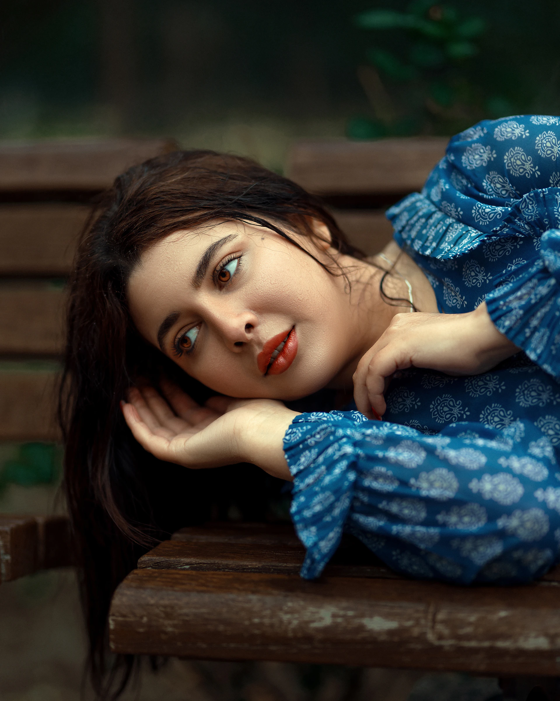 a woman in a blue dress laying on a wooden bench