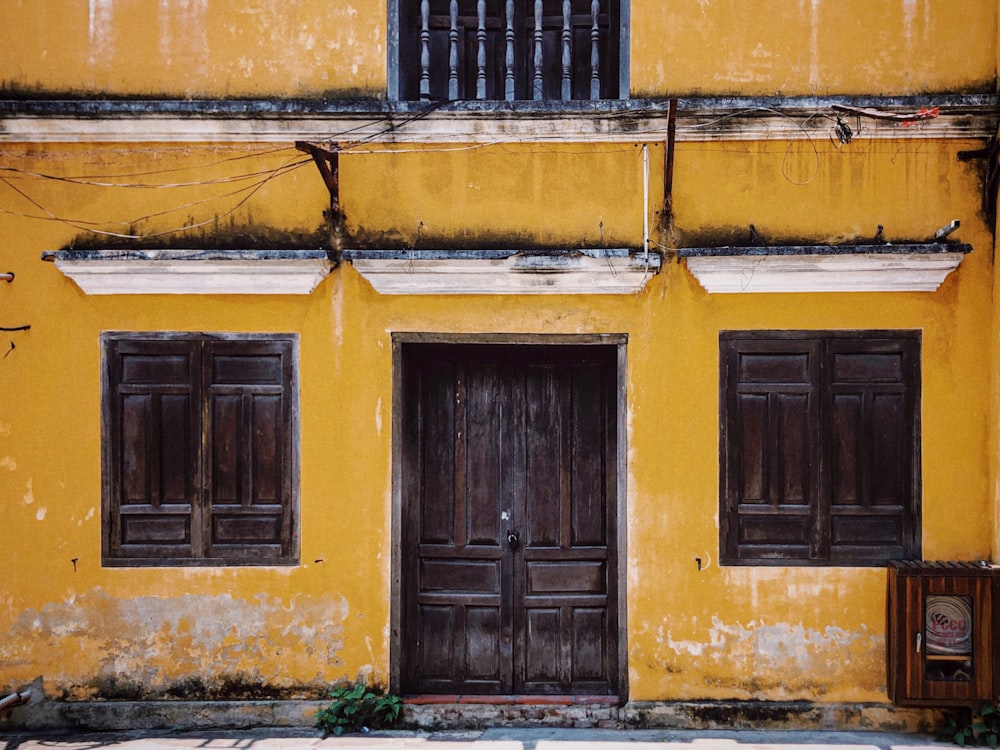 a yellow building with two brown doors and windows