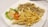 A white plate containing crispy fried chicken strips, a serving of golden French fries, and a side salad with shredded cabbage, lettuce, sliced cucumber, and a tomato slice topped with a dollop of creamy dressing.