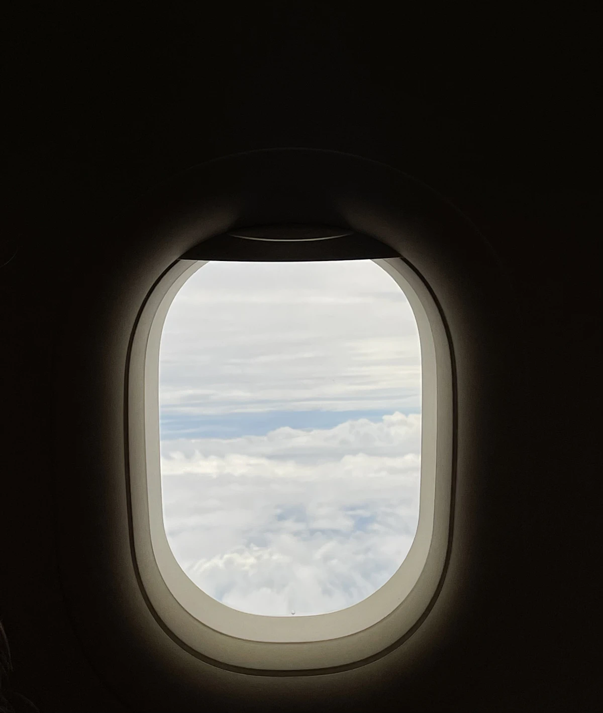 Airplane window view during flight with clouds and sky