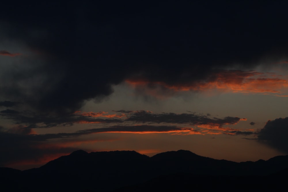 the sun is setting over the mountains with dark clouds