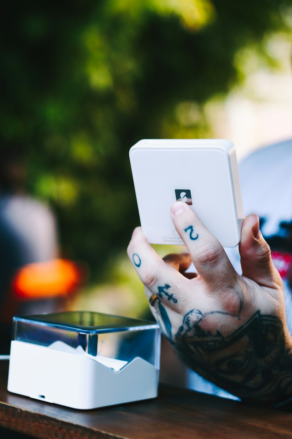 a tattooed hand holding up a white device