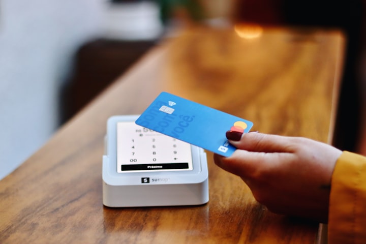Mão aproximando um cartão de crédito azul da maquininha de pagamento sobre um balcão de madeira