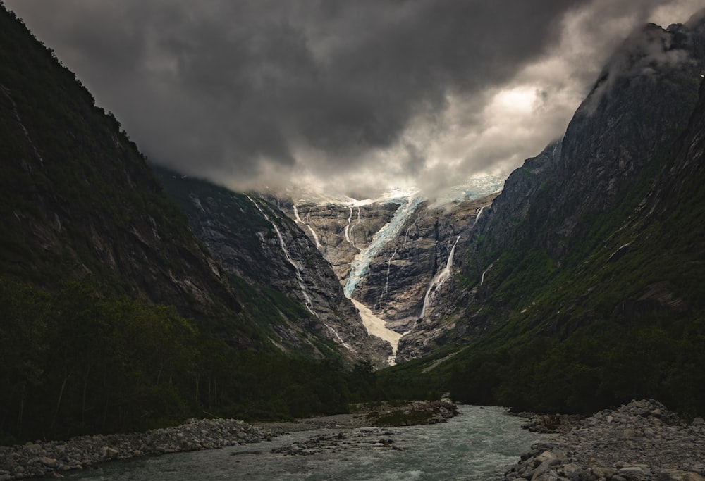 a river flowing between two mountains under a cloudy sky