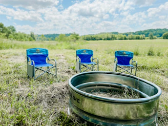 A sturdy folding metal chair set up beside a campfire in a forest clearing at sunset