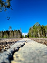 A close-up of a freshly paved asphalt road under a clear blue sky.