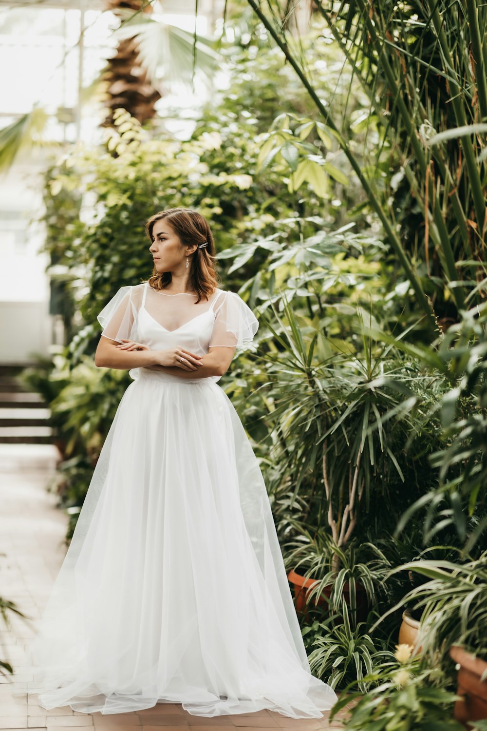 a woman in a white dress standing in a greenhouse