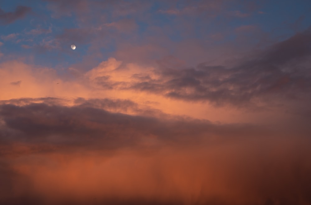 a cloudy sky with a half moon in the distance