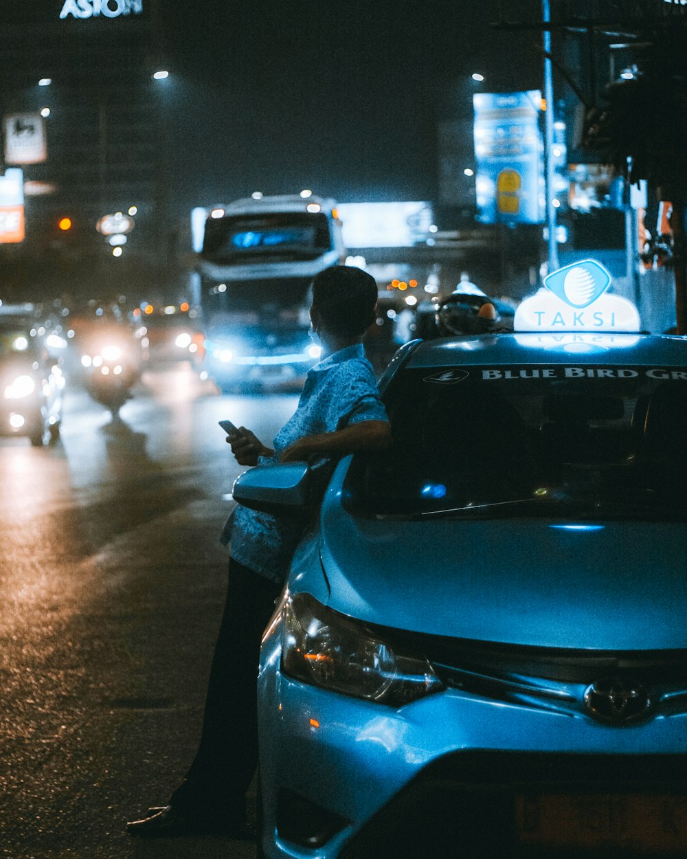 um homem em pé ao lado de um carro em uma rua à noite