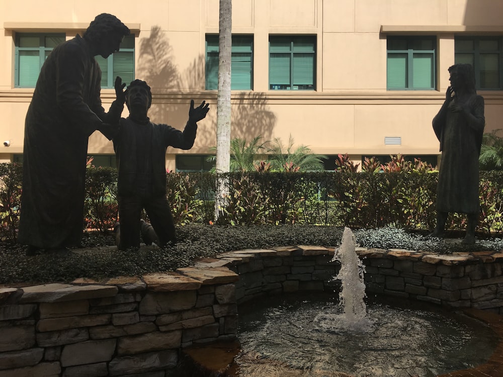 Una estatua de un hombre y dos niños frente a una fuente