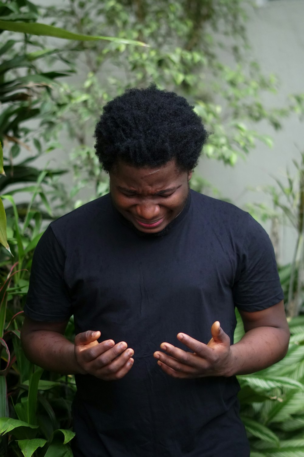 a man standing in front of a bush holding his hands together