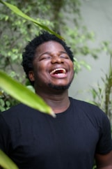 a man laughing while standing in front of a plant